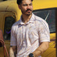 A rugged man with a stylish beard and tattooed arm models the HowdyHo Sunshine Paisley shirt. The shirt's light paisley pattern adds a touch of understated elegance to his laid-back look. He's casually leaning against a vintage yellow truck, with a black watch on his wrist, embodying a blend of masculinity and sophistication.